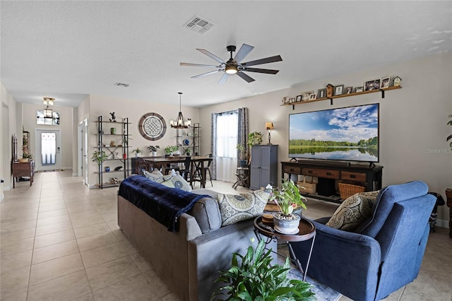 tiled living room featuring ceiling fan with notable chandelier and a textured ceiling