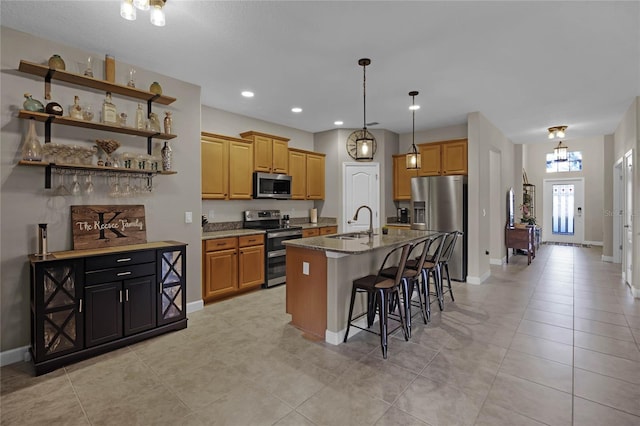 kitchen with a breakfast bar, a kitchen island with sink, dark stone countertops, light tile patterned floors, and appliances with stainless steel finishes