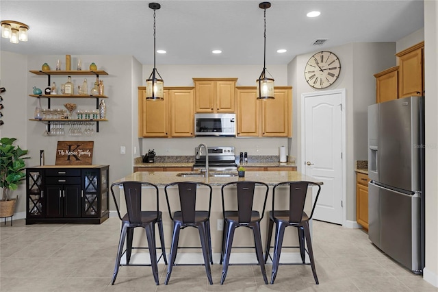 kitchen featuring appliances with stainless steel finishes, a kitchen breakfast bar, light stone counters, a kitchen island with sink, and sink