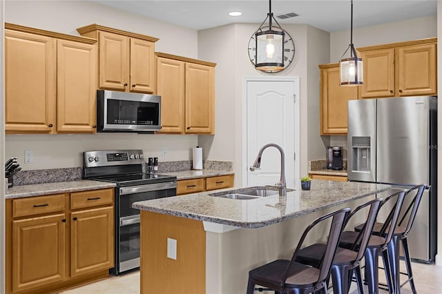 kitchen featuring a center island with sink, sink, hanging light fixtures, light stone counters, and stainless steel appliances