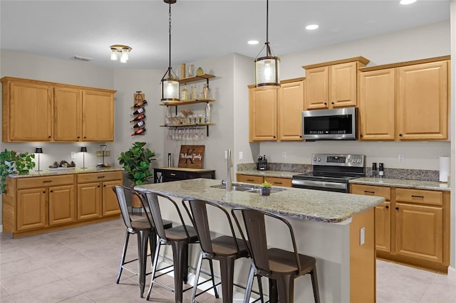 kitchen with pendant lighting, sink, light stone countertops, an island with sink, and stainless steel appliances