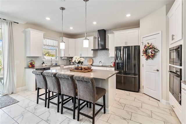 kitchen with oven, wall chimney range hood, stainless steel refrigerator with ice dispenser, a kitchen island, and white cabinetry