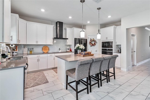 kitchen featuring white cabinetry, sink, wall chimney range hood, a kitchen island, and black appliances