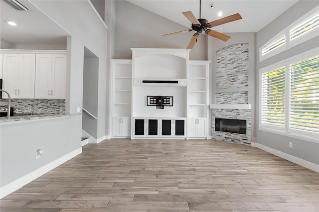 unfurnished living room with a tile fireplace, light hardwood / wood-style floors, ceiling fan, and a high ceiling