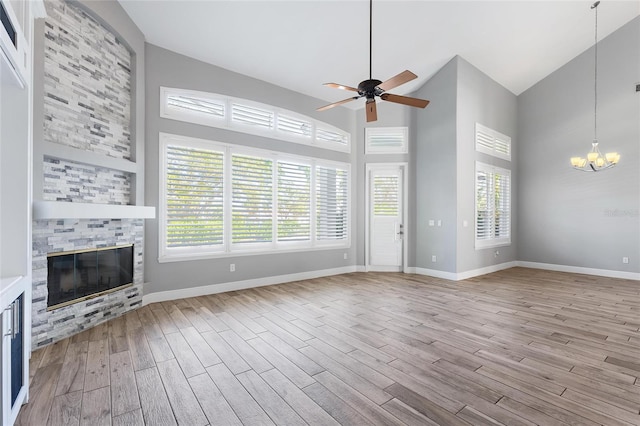 unfurnished living room featuring high vaulted ceiling, ceiling fan with notable chandelier, a fireplace, and light wood-type flooring