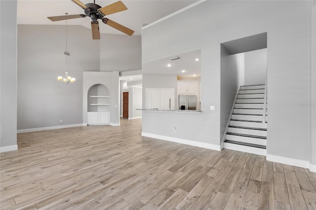 unfurnished living room with high vaulted ceiling, ceiling fan with notable chandelier, and light hardwood / wood-style floors