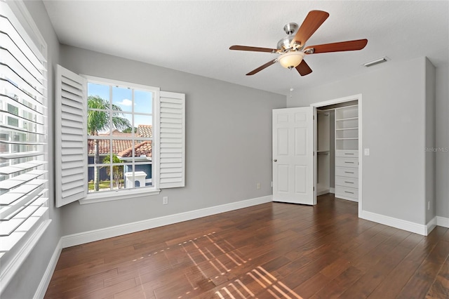 unfurnished bedroom with a spacious closet, dark wood-type flooring, a closet, and ceiling fan