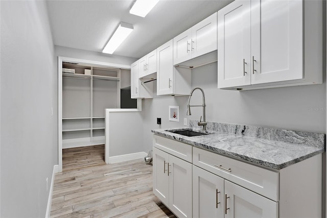 kitchen featuring white cabinetry, sink, light stone counters, and light hardwood / wood-style floors