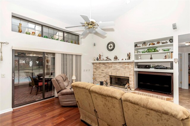 living area featuring a towering ceiling, a brick fireplace, a ceiling fan, and wood finished floors