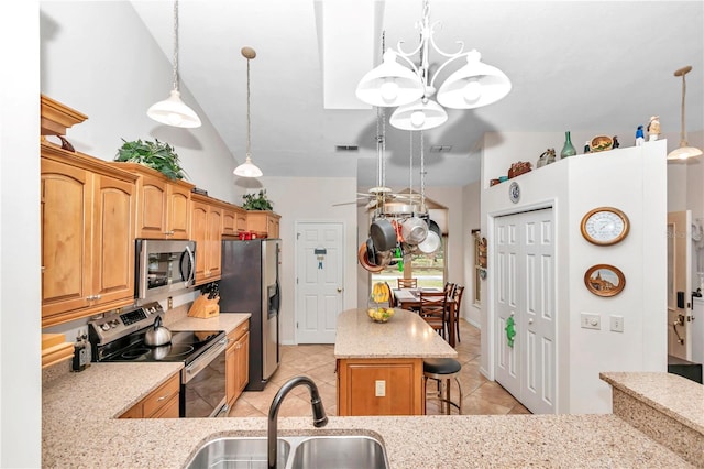 kitchen with a sink, a kitchen breakfast bar, appliances with stainless steel finishes, light stone countertops, and decorative light fixtures