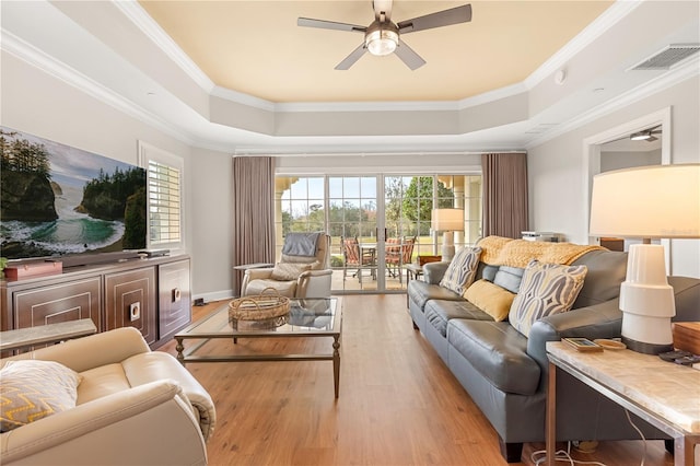 living room featuring a raised ceiling, ceiling fan, ornamental molding, and light hardwood / wood-style flooring