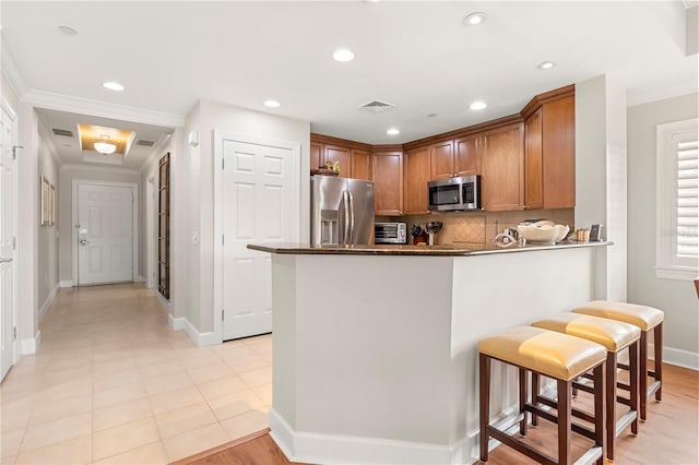 kitchen featuring a kitchen breakfast bar, stainless steel appliances, kitchen peninsula, light tile patterned floors, and ornamental molding