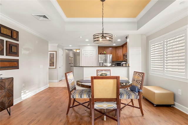 dining room featuring a raised ceiling, a chandelier, ornamental molding, and light wood-type flooring