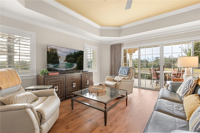 living room featuring light hardwood / wood-style floors, ceiling fan, crown molding, and a tray ceiling