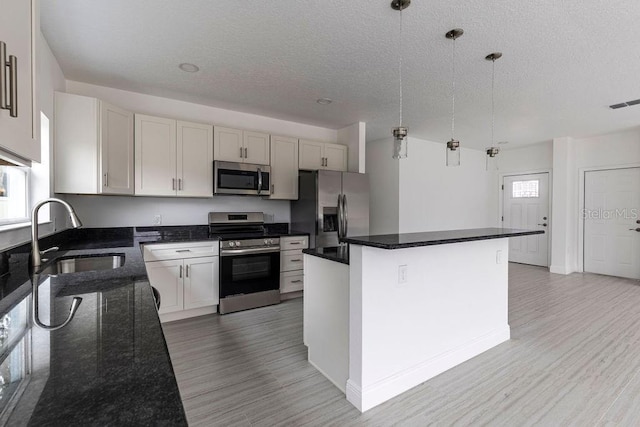 kitchen with white cabinetry, stainless steel appliances, hanging light fixtures, a kitchen island, and sink