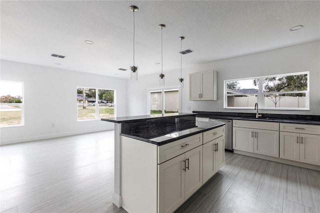 kitchen with dishwasher, dark stone countertops, a center island, sink, and hanging light fixtures