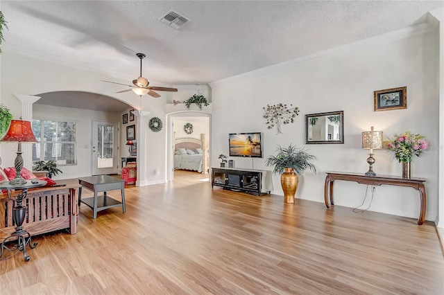 living room with ceiling fan, light hardwood / wood-style flooring, a textured ceiling, and ornamental molding