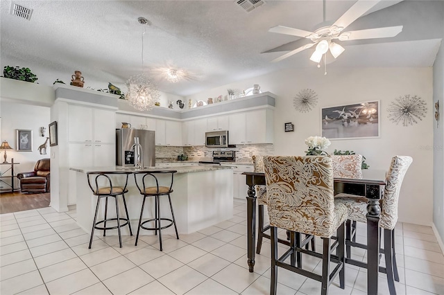 kitchen with a kitchen breakfast bar, tasteful backsplash, a textured ceiling, stainless steel appliances, and white cabinetry