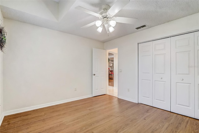 unfurnished bedroom featuring ceiling fan, a closet, light hardwood / wood-style floors, and a textured ceiling