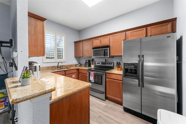 kitchen featuring kitchen peninsula, appliances with stainless steel finishes, a kitchen bar, light stone countertops, and sink