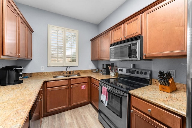 kitchen with appliances with stainless steel finishes, light wood-type flooring, light stone counters, and sink