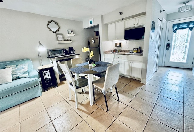 kitchen featuring sink, light tile patterned floors, stainless steel refrigerator, and white cabinets