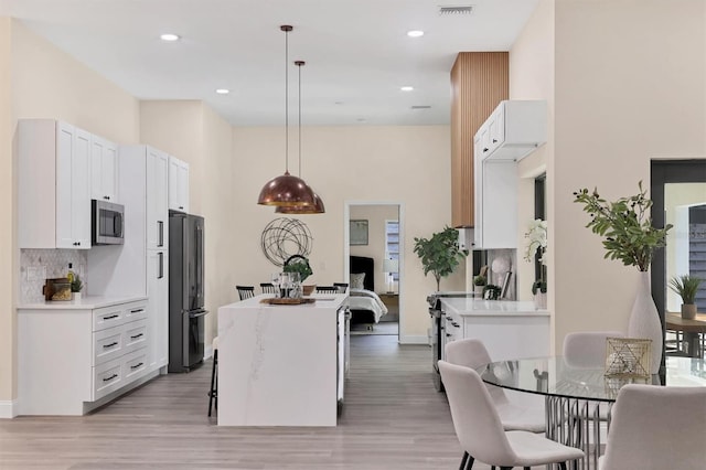 kitchen with a center island, hanging light fixtures, decorative backsplash, white cabinetry, and stainless steel appliances