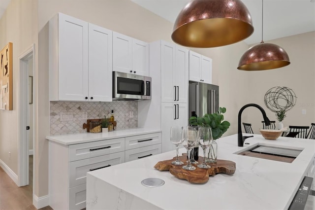 kitchen featuring sink, hanging light fixtures, tasteful backsplash, white cabinets, and appliances with stainless steel finishes