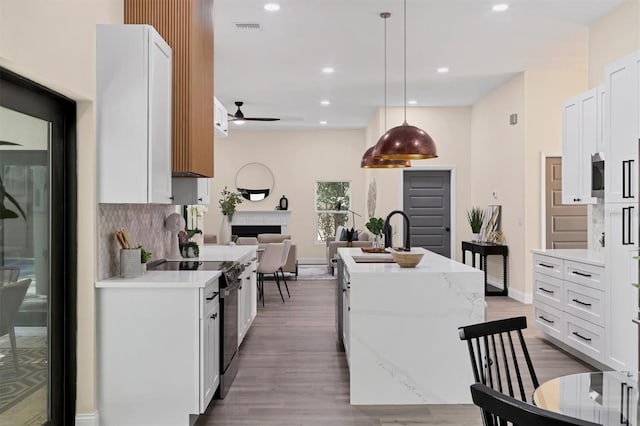 kitchen with white cabinetry, sink, backsplash, decorative light fixtures, and a kitchen island with sink