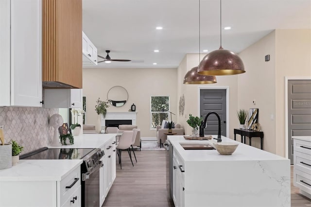 kitchen featuring stainless steel appliances, ceiling fan, a kitchen island with sink, decorative light fixtures, and white cabinets