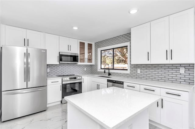 kitchen featuring appliances with stainless steel finishes, sink, white cabinets, backsplash, and a center island