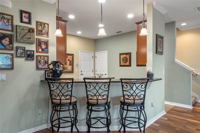 kitchen with kitchen peninsula, a breakfast bar, crown molding, decorative light fixtures, and dark hardwood / wood-style floors