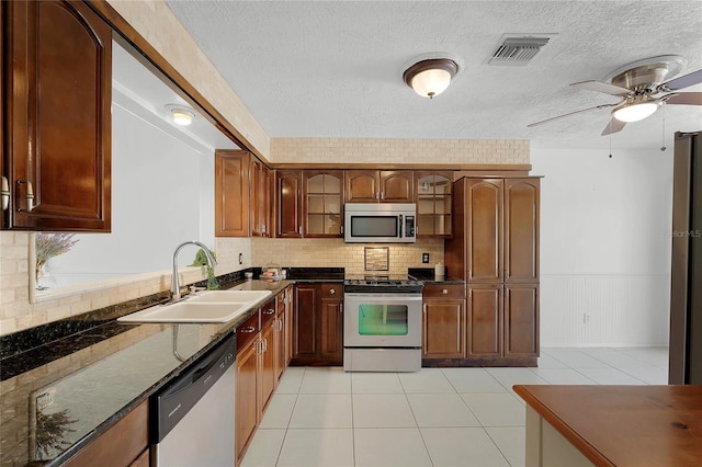 kitchen featuring ceiling fan, sink, appliances with stainless steel finishes, light tile patterned floors, and dark stone counters