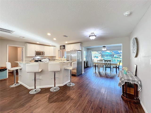 kitchen with dark wood-type flooring, white cabinets, a kitchen breakfast bar, a textured ceiling, and appliances with stainless steel finishes