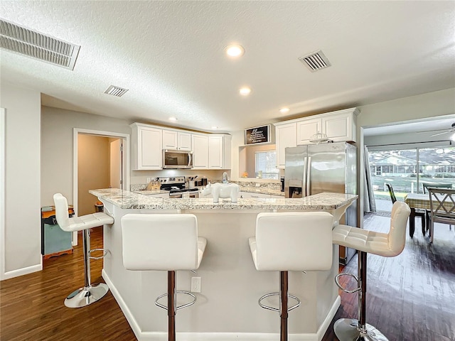 kitchen featuring white cabinets, a kitchen breakfast bar, dark hardwood / wood-style floors, a textured ceiling, and appliances with stainless steel finishes