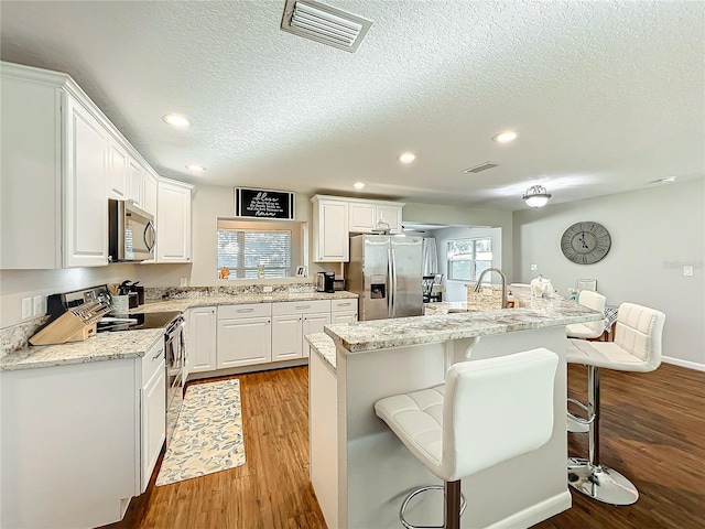 kitchen with a center island, white cabinets, a kitchen breakfast bar, light wood-type flooring, and appliances with stainless steel finishes