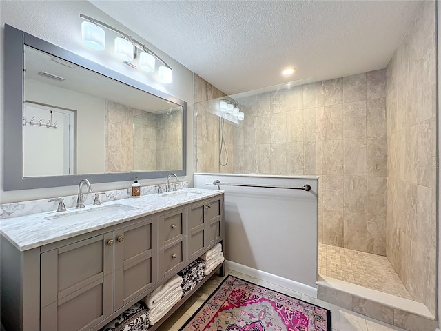 bathroom with tile patterned flooring, vanity, a tile shower, and a textured ceiling