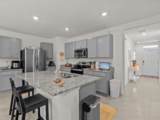 kitchen with a kitchen bar, a kitchen island with sink, sink, light stone counters, and stainless steel appliances