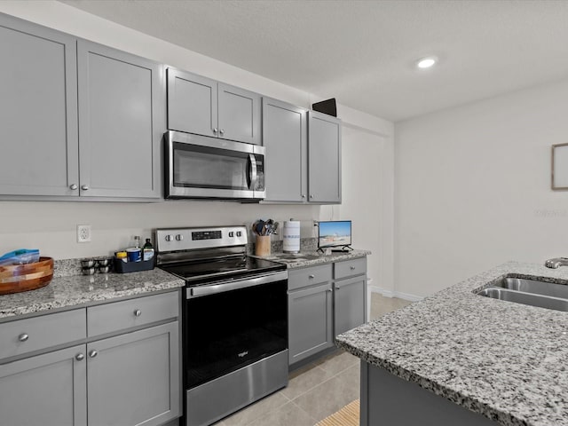 kitchen with gray cabinetry, light stone countertops, sink, stainless steel appliances, and light tile patterned floors