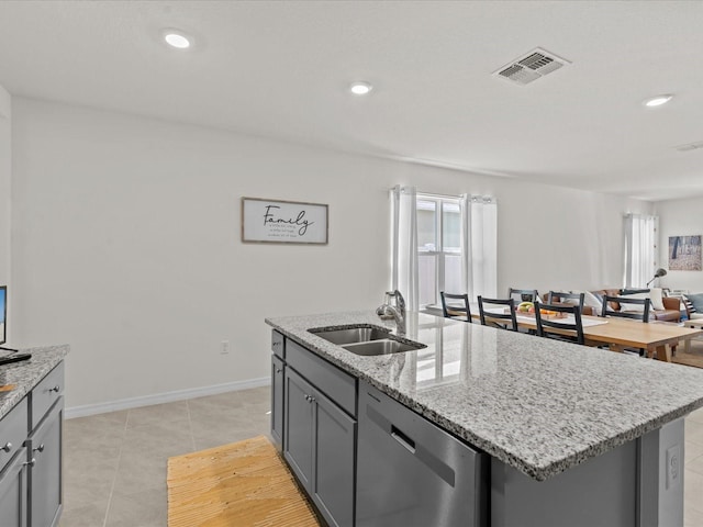 kitchen featuring a center island with sink, sink, stainless steel dishwasher, gray cabinets, and light stone counters