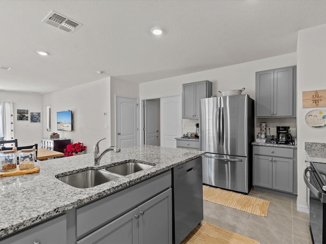 kitchen with light stone counters, gray cabinets, sink, and stainless steel appliances