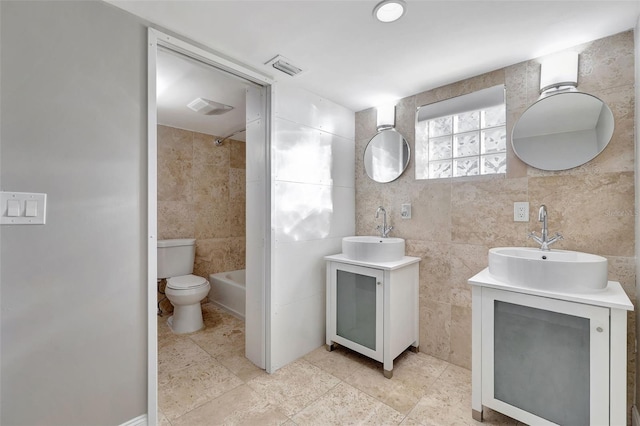 full bathroom featuring toilet, vanity, tile walls, and washtub / shower combination