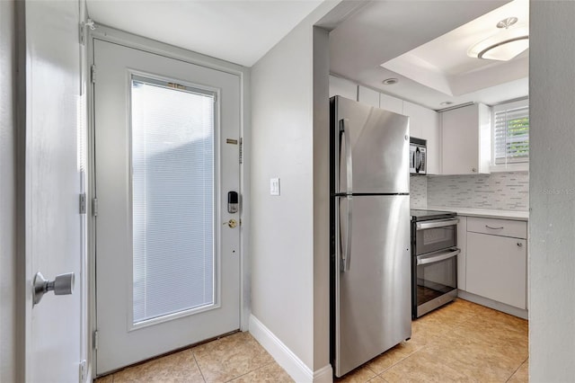 kitchen featuring tasteful backsplash, white cabinets, light tile patterned floors, and appliances with stainless steel finishes