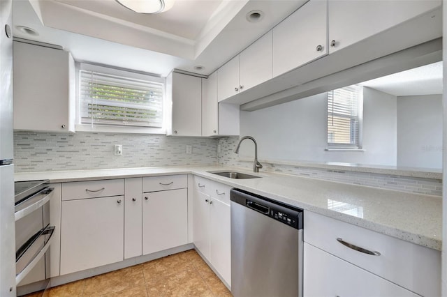 kitchen featuring stainless steel dishwasher, sink, white cabinets, and backsplash