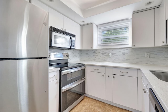 kitchen featuring stainless steel appliances, tasteful backsplash, white cabinets, light stone counters, and light tile patterned flooring