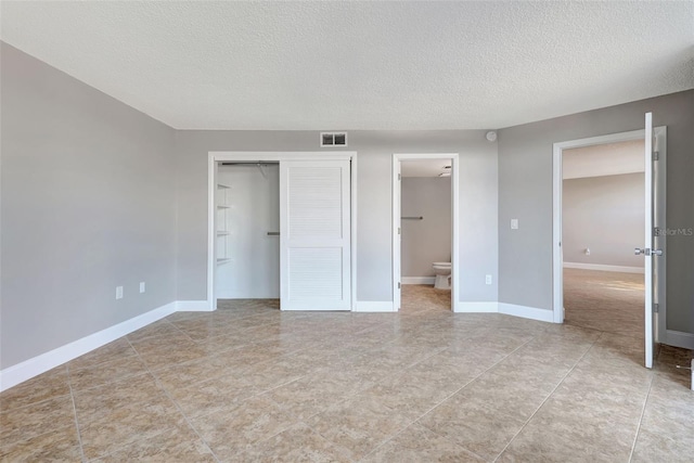 unfurnished bedroom featuring a closet, light tile patterned flooring, a textured ceiling, and ensuite bath