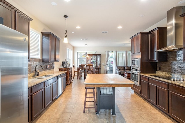 kitchen featuring appliances with stainless steel finishes, wall chimney exhaust hood, tasteful backsplash, sink, and hanging light fixtures