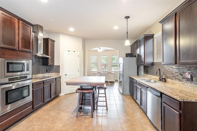 kitchen with stainless steel appliances, tasteful backsplash, hanging light fixtures, wall chimney exhaust hood, and sink