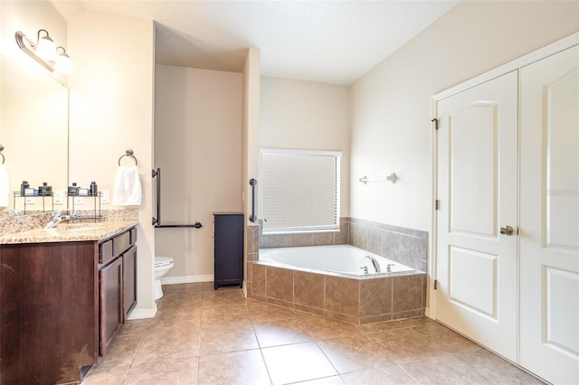 bathroom featuring toilet, tile patterned flooring, a relaxing tiled tub, and vanity