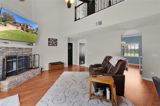 living room featuring ceiling fan, a high ceiling, a brick fireplace, ornamental molding, and hardwood / wood-style flooring